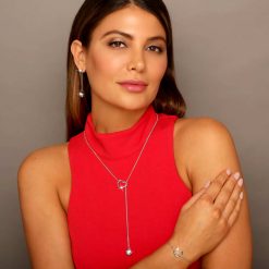 Millennial woman in red wears Twisted Heart & Orb lariet Necklace Rhodium over Sterling Silver with 2 clear diamond cut CZ stones Heart bracelet on her hand and orb earrings designed by ARY D'PO