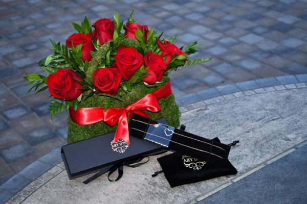 ARY DPO Hearts and Orbs necklace placed with the branded packaging and a beautiful bouquet of red roses 