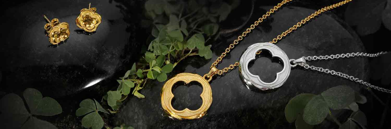 ARY D'PO Four Leaf Clover Jewelry Collection Quatrefoil ornament in gold and silver beautifully arranged on black wet stones surrounded by green clover plants.
