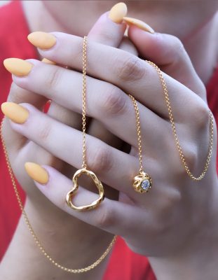 Heart necklace as symbolic jewelry is presented by a young woman wearing red cloth holding in her hand the 18K Gold plated sterling silver Twisted Heart & Orb lariat necklace by ARY D'PO as a symbol of love.