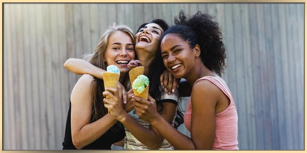 Three young women are posing together holding ice cremes highlighting their friendship.