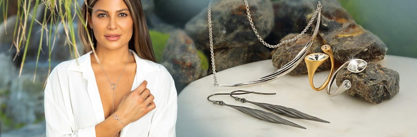 A young beautiful woman wearing a white shirt is showcasing the arydpo heart necklace and bracelet in silver. The arydpo mixed jewelry is in the background.