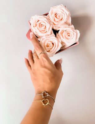 Twisted Heart Bracelets in gold and silver on a hand with pink roses in the background