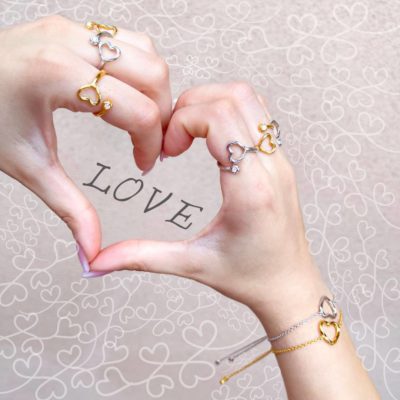 arydpo Heart & Orb rings and Heart bracelets on hands making heart shape. Little hearts drawn on the surface surrounding the hands and the word LOVE is written in the middle of the heart shape made with hands.