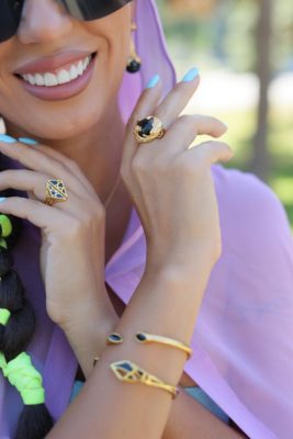 ARY D'PO Black Jewel ring and earrings and Black Enamel on gold Dream bracelet and ring showcased by a beautiful woman. She is wearing light purple cape and smiling. 